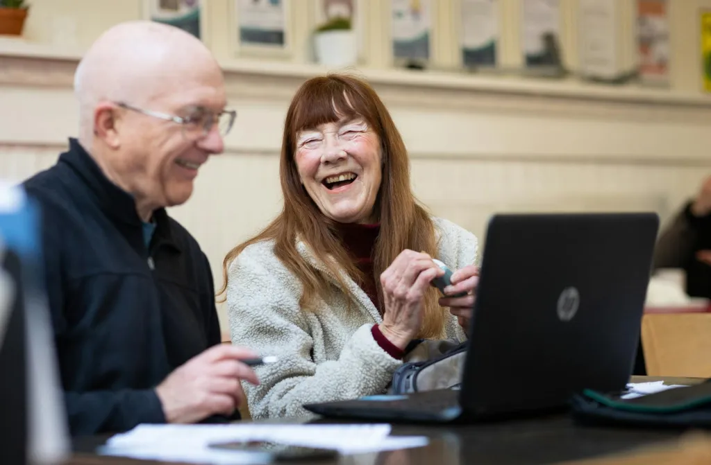 Two people smiling at table in front of laptop.
