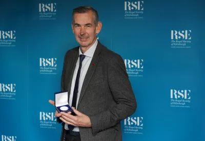 Andy Baker in suit and tie holding medal.