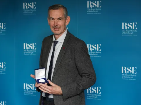 Andy Baker in suit and tie holding medal.